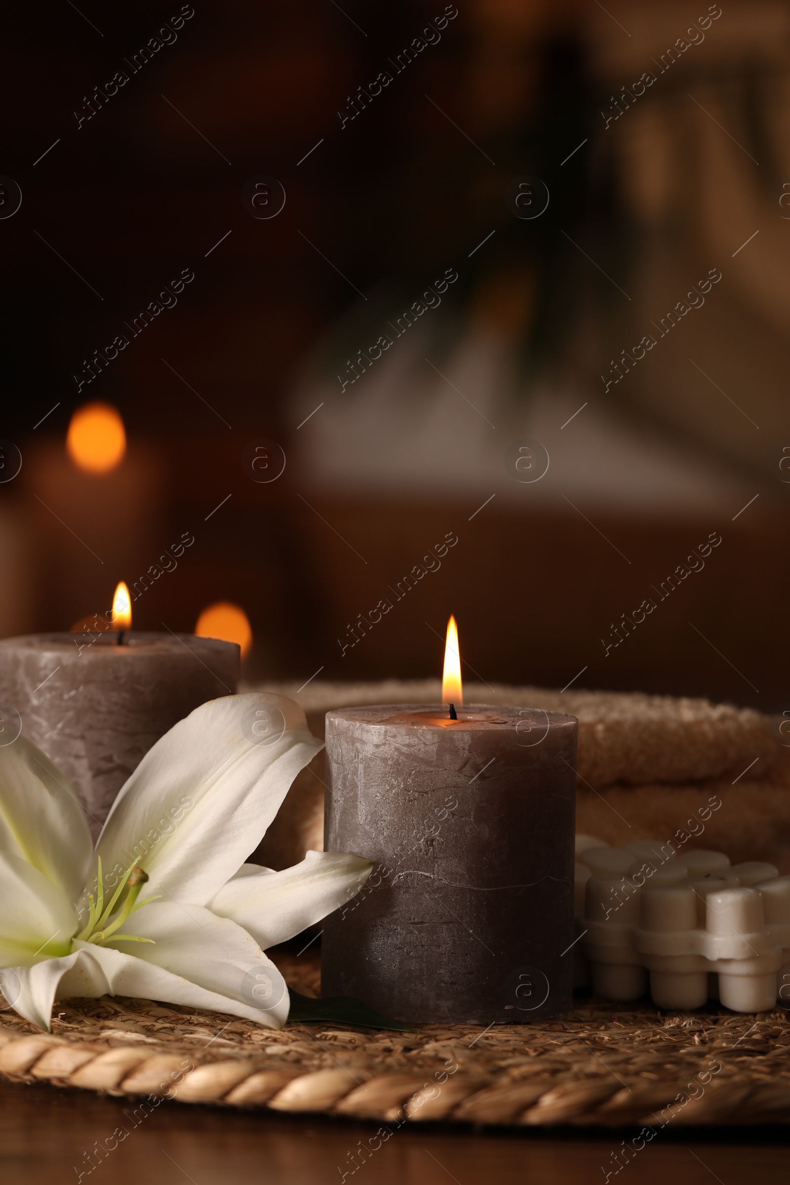 Photo of Spa composition with burning candles, lily flower and towels on wooden table in wellness center, space for text