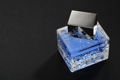 Photo of Blue men's perfume in bottle on black background, space for text