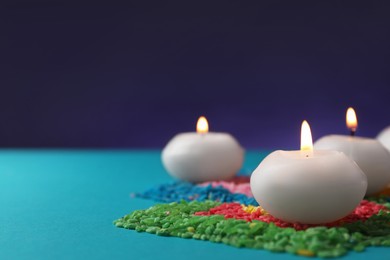 Photo of Diwali celebration. Burning candles and colorful rangoli on light blue background, closeup. Space for text