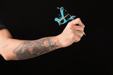 Photo of Professional tattoo artist with machine on black background, closeup