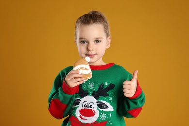 Photo of Cute little girl with Christmas gingerbread cookie on orange background