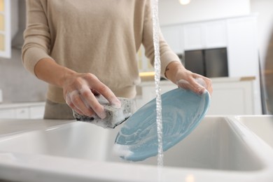 Woman washing plate above sink in modern kitchen, closeup