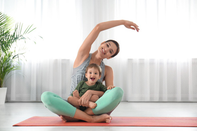 Young woman doing exercise with her son indoors. Home fitness