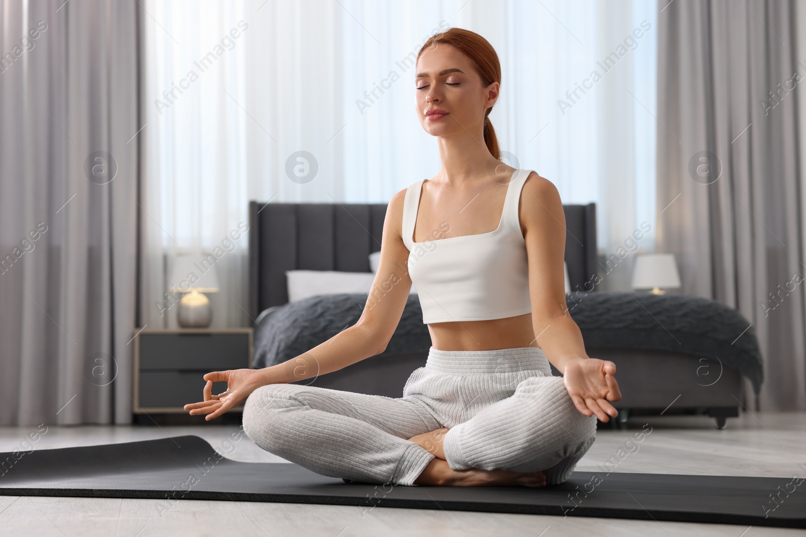 Photo of Beautiful young woman practicing Padmasana on yoga mat at home. Lotus pose