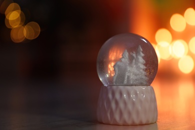 Snow globe on wooden table against blurred background, space for text. Bokeh effect