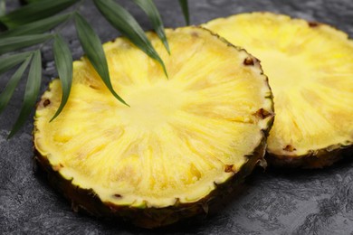 Photo of Slices of tasty ripe pineapple and green leaves on black textured table, closeup
