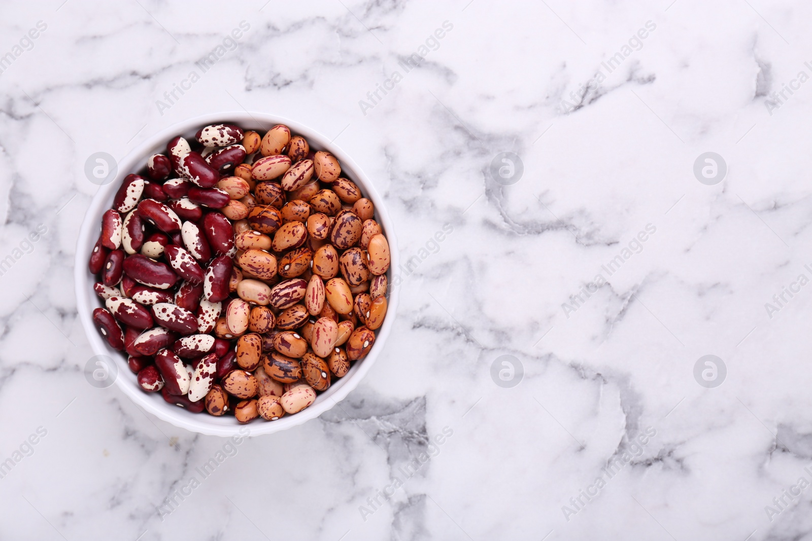 Photo of Different kinds of dry kidney beans in bowl on white marble table, top view. Space for text