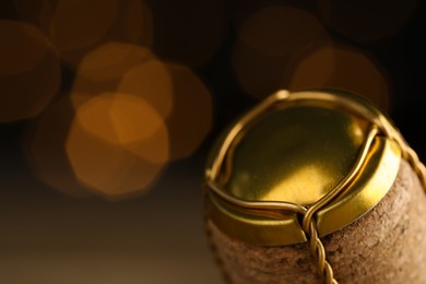 Closeup view of sparkling wine cork and muselet cap against blurred festive lights, space for text. Bokeh effect