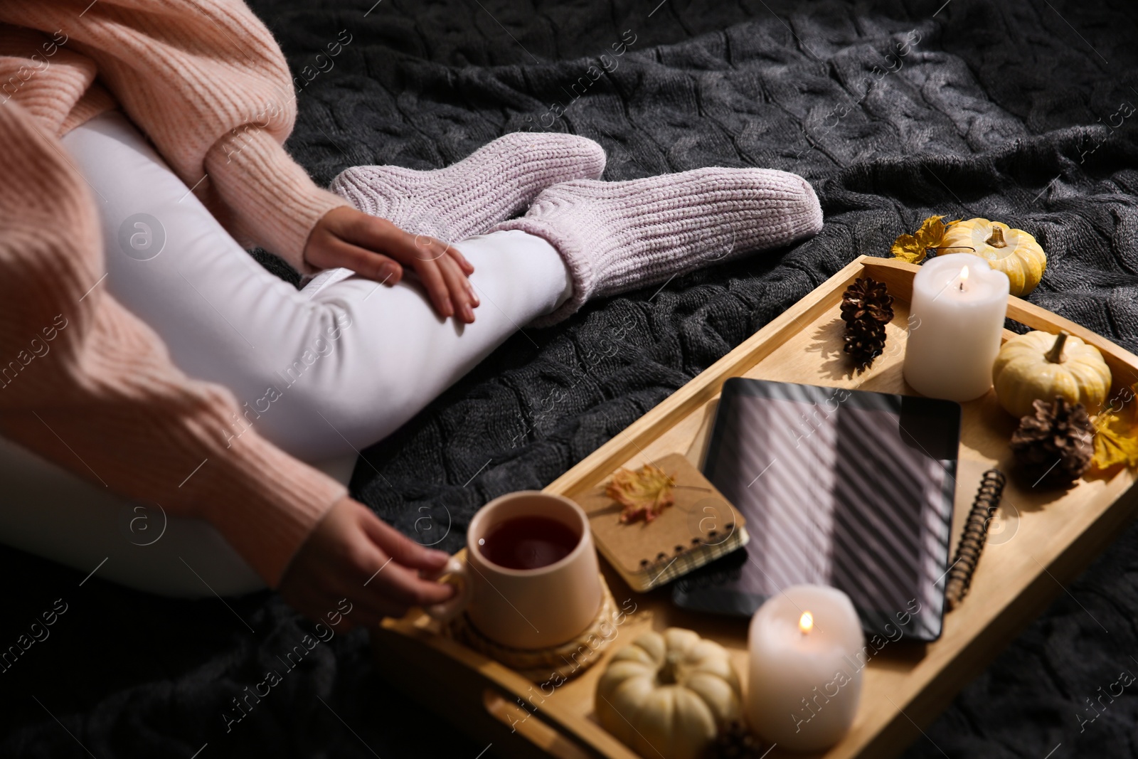 Photo of Woman in warm socks relaxing on knitted plaid, closeup