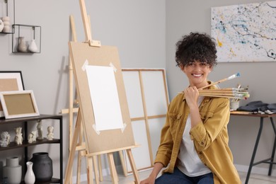 Photo of Happy woman with brushes near easel in studio