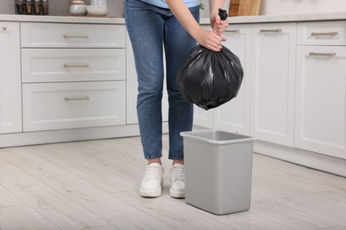 Photo of Woman taking garbage bag out of trash bin in kitchen, closeup