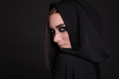 Photo of Mysterious witch in mantle with hood on black background
