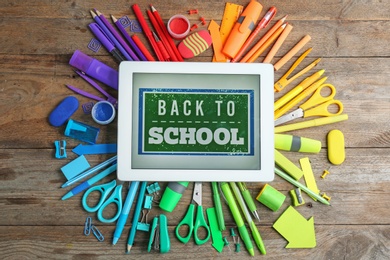 Tablet with phrase "BACK TO SCHOOL" and different stationery on wooden background, flat lay