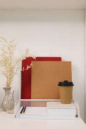 Photo of Books, dry flowers and paper cup of coffee on white wooden table