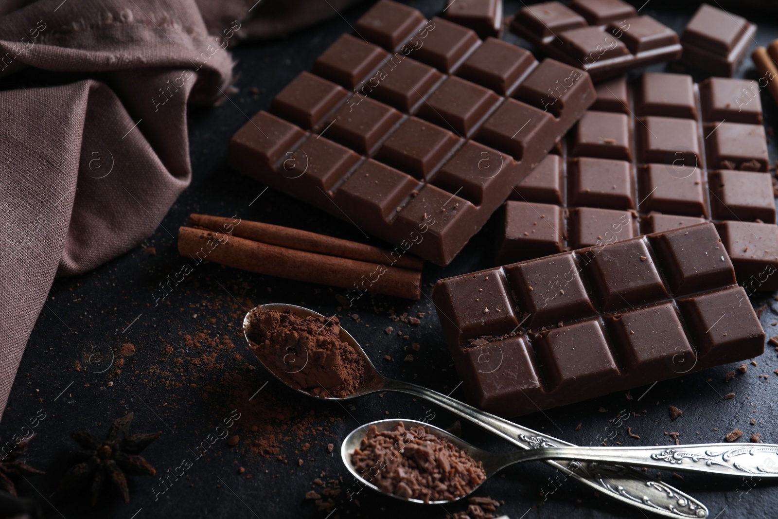 Photo of Tasty milk chocolate and spoons with cocoa powder on black table