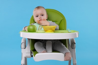 Photo of Cute little baby eating healthy food in high chair on light blue background