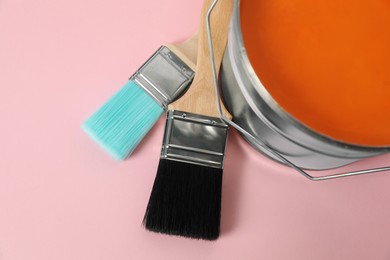 Bucket of orange paint and brushes on pink background, closeup
