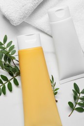 Tubes of face cleansing products, towel and green leaves on white marble table, flat lay