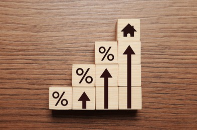 Image of Mortgage rate rising illustrated by upward arrows, cubes with percent signs and house icon on wooden background, flat lay