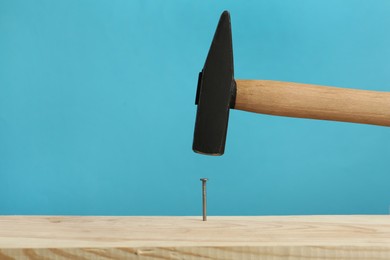 Photo of Hammering nail into wooden surface against light blue background, space for text