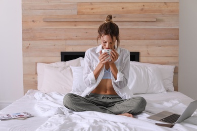 Photo of Young happy woman with cup of aromatic coffee on bed at home. Lazy morning