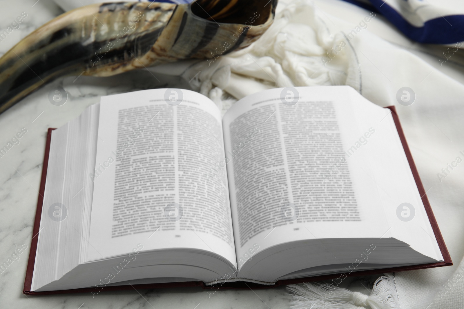 Photo of Tallit, shofar and open Torah on white marble table, closeup. Rosh Hashanah celebration