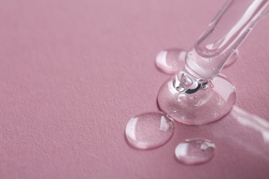 Dripping cosmetic serum from pipette onto pink background, macro view. Space for text