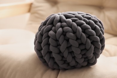 Photo of Dark grey chunky knitted pillow on beige sofa, closeup