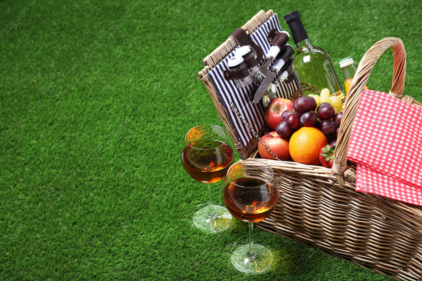 Photo of Wicker picnic basket with different products on green grass, space for text