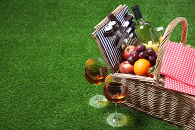 Wicker picnic basket with different products on green grass, space for text