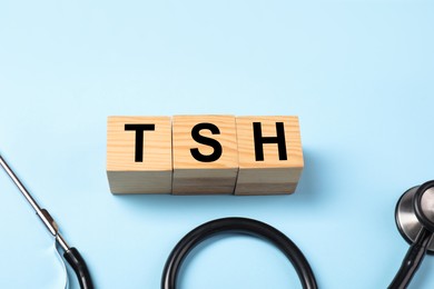 Photo of Endocrinology. Stethoscope and wooden cubes with thyroid hormones on light blue background. Space for text