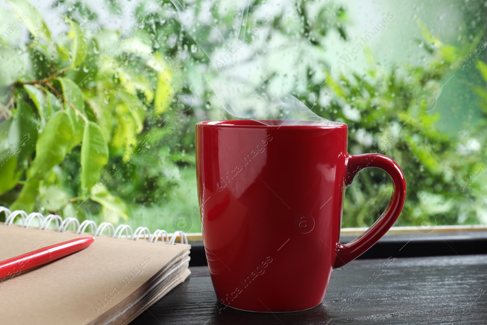 Photo of Cup of hot drink and notebook on wooden windowsill. Rainy weather