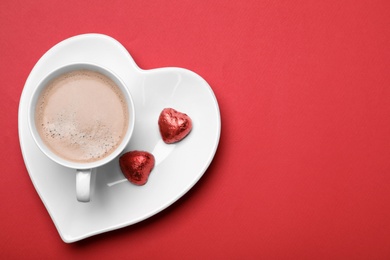 Cup of coffee and chocolate candies on red background, top view with space for text. Valentine's day breakfast