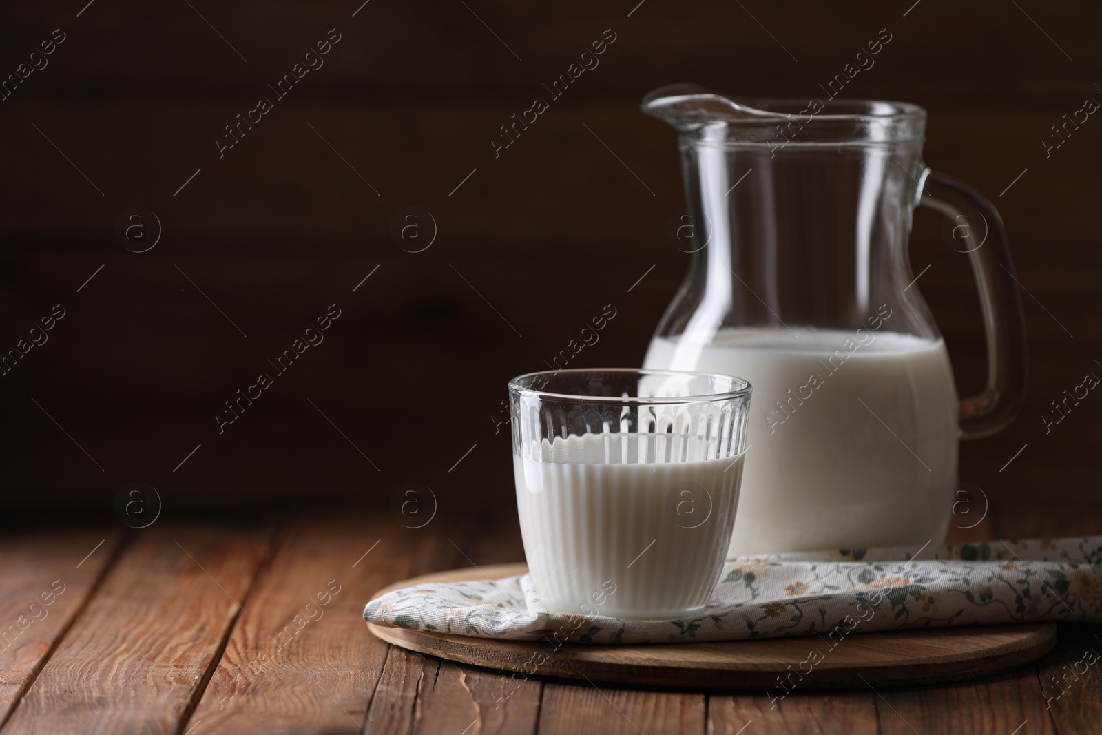 Photo of Tasty fresh milk in jug and glass on wooden table, space for text