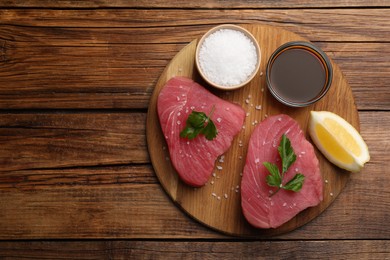 Photo of Raw tuna fillets with parsley, lemon and soy sauce on wooden table, top view. Space for text