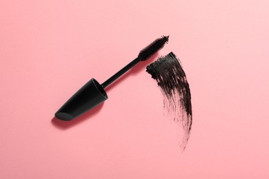 Photo of Mascara wand and smear on pink background, top view. Makeup product