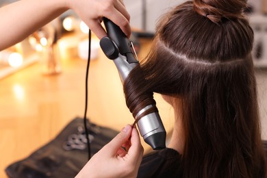 Hairdresser using curling hair iron while working with woman in salon, closeup