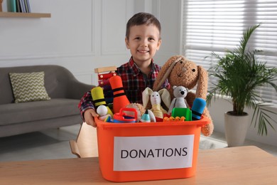 Photo of Cute little boy holding donation box with toys at home