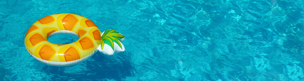 Image of Bright inflatable pineapple ring floating in swimming pool on sunny day, space for text. Banner design