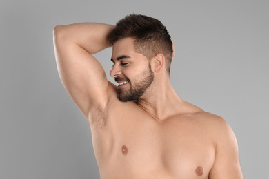 Young man showing hairless armpit after epilation procedure on grey background