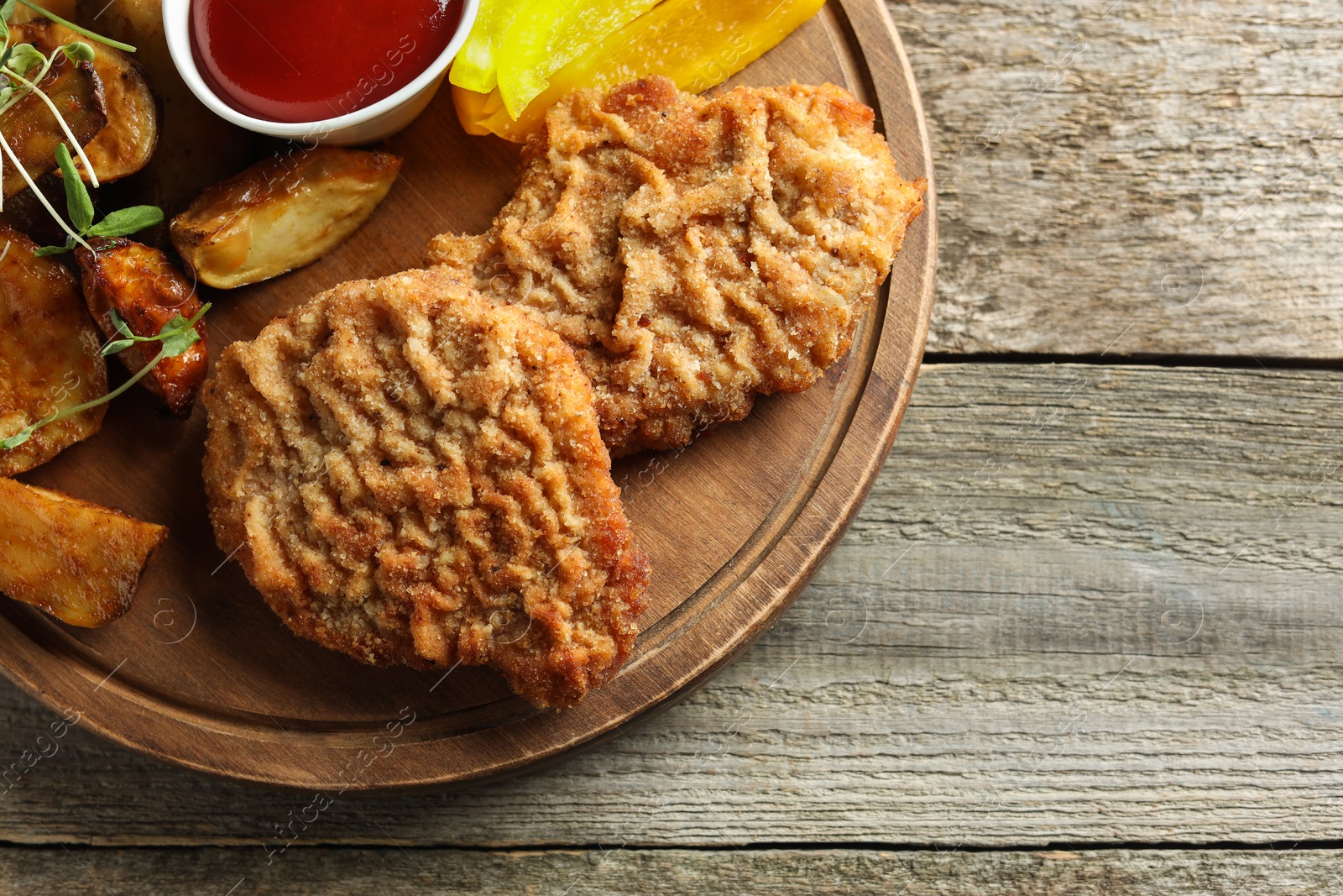 Photo of Tasty schnitzels served with potatoes, ketchup and pepper on wooden table, top view. Space for text