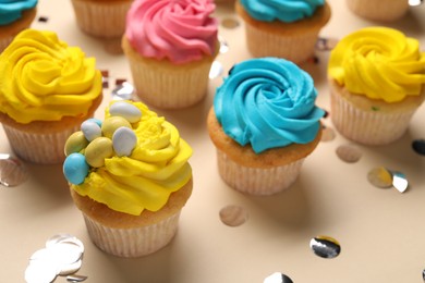 Delicious cupcakes with bright cream and confetti on beige background, closeup