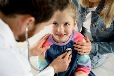 Photo of Mother and daughter having appointment with doctor. Pediatrician examining patient with stethoscope