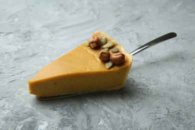 Photo of Cake server with piece of delicious pie with hazelnuts and pumpkin seeds on grey textured table