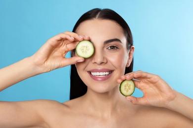 Photo of Woman holding pieces of cucumber on light blue background. Spa treatment