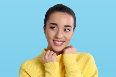 Beautiful young woman wearing yellow warm sweater on light blue background
