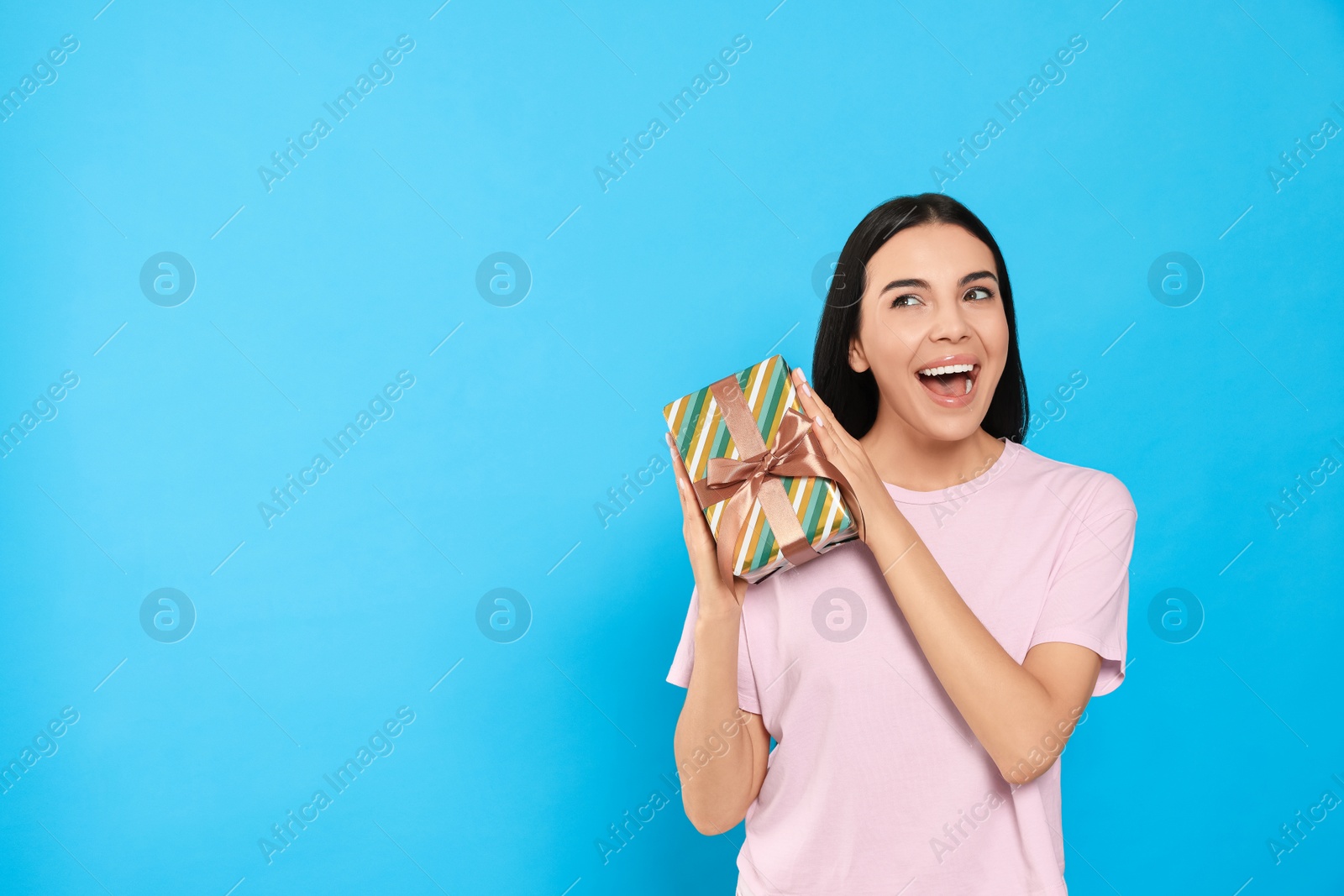 Photo of Emotional young woman holding gift box on light blue background, space for text