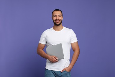 Smiling young man with laptop on lilac background