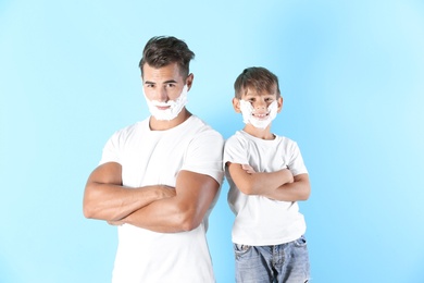 Father and son with shaving foam on faces against color background