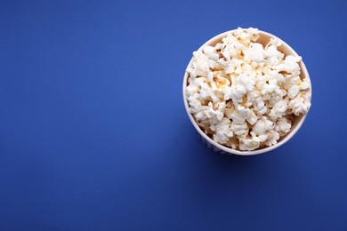 Photo of Bucket of tasty popcorn on blue background, above view. Space for text
